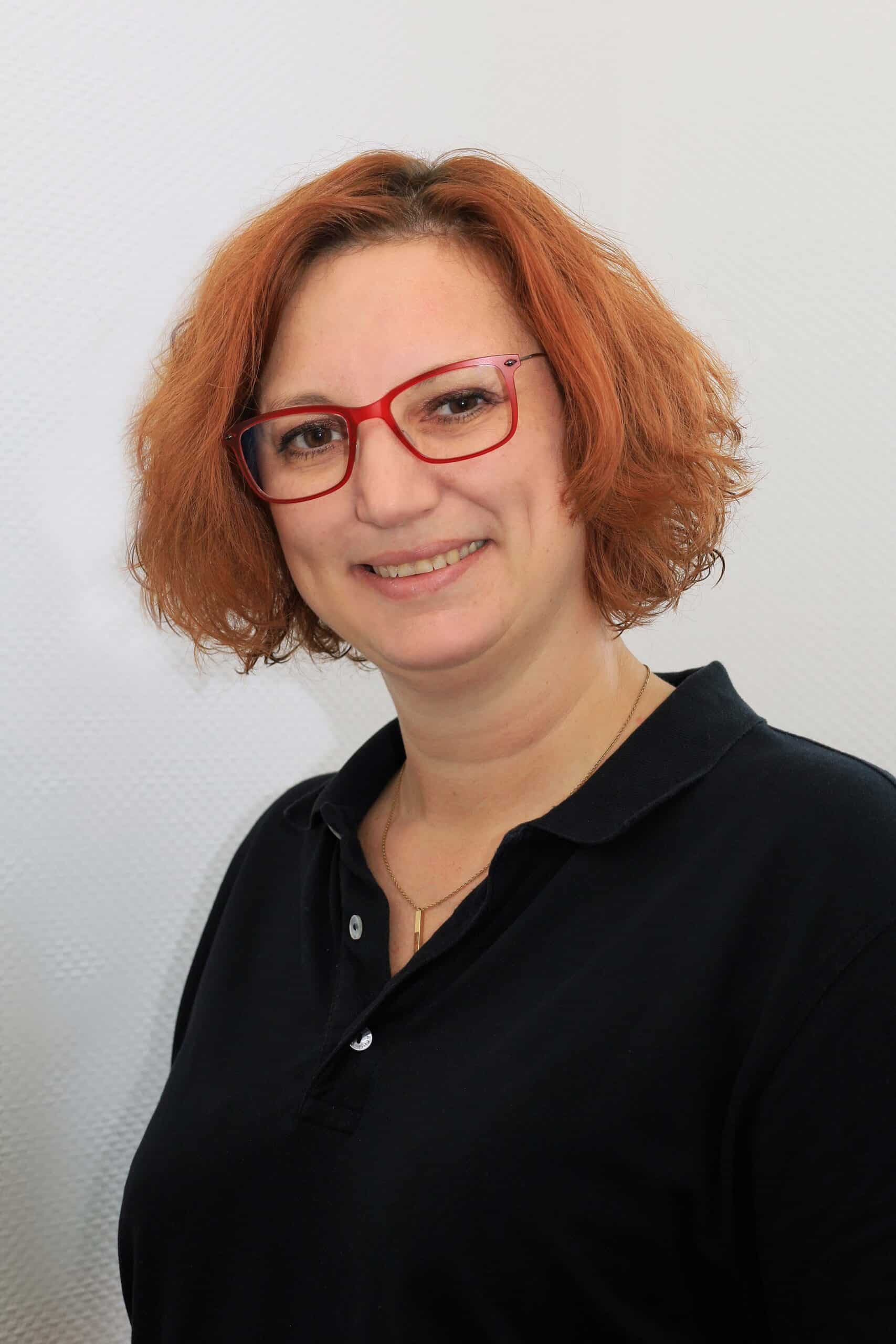 Frau mit roten Haaren und Brille vor weißem Hintergrund.