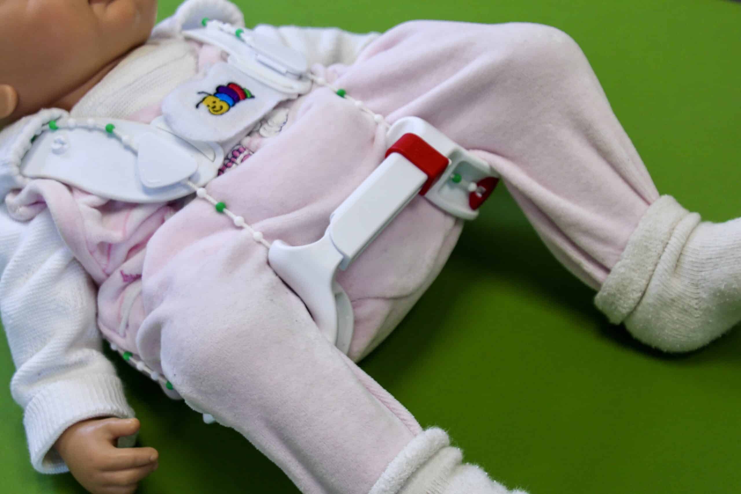 Baby mit Hüftbeugeschiene in Kinderbett auf grünem Untergrund.